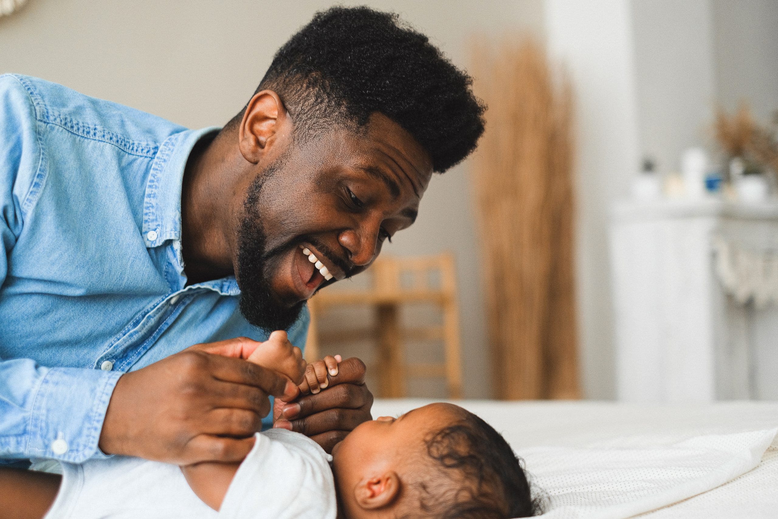 An african american dad holds his 6-month old's hands and sings a song while looking lovingly into his eyes.