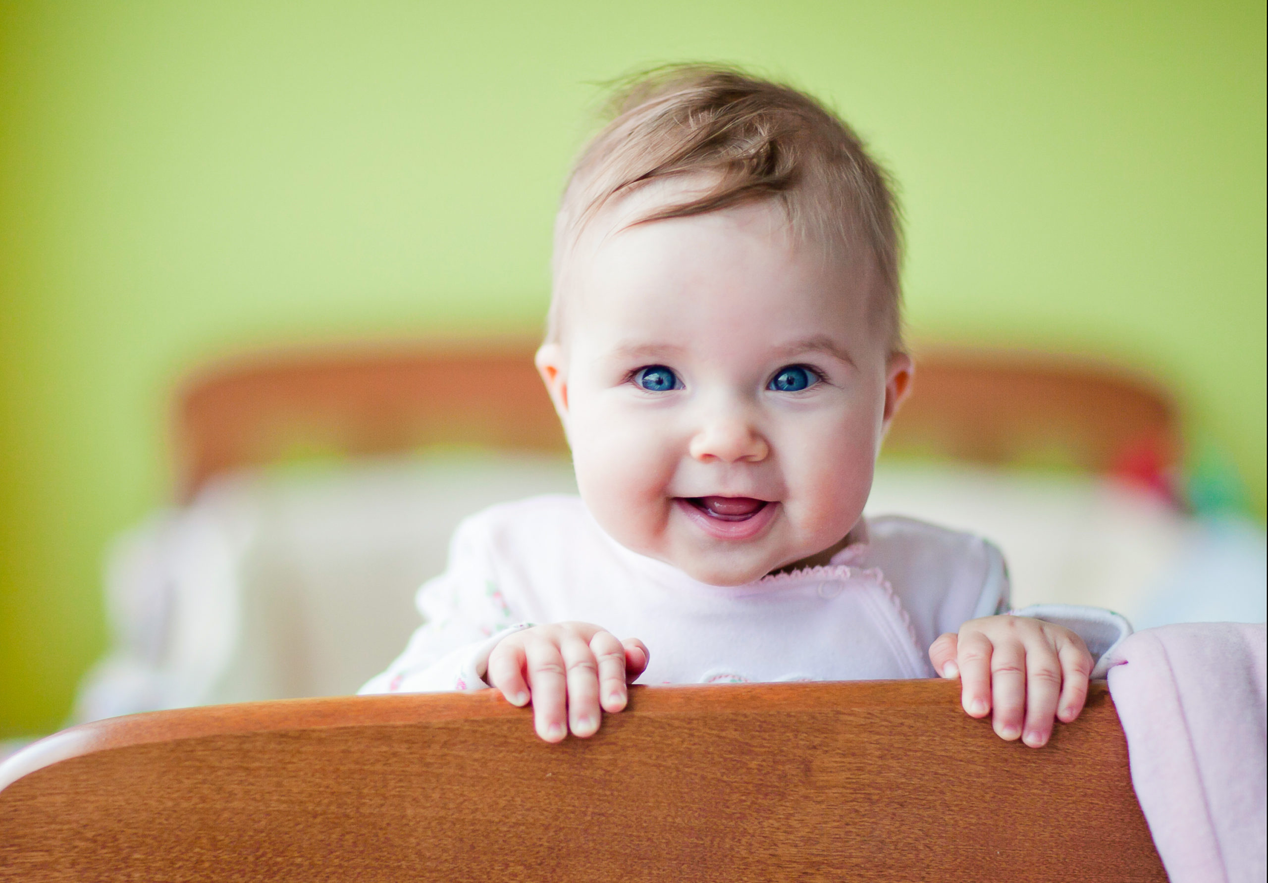 A very cute baby standing in her crib smiling